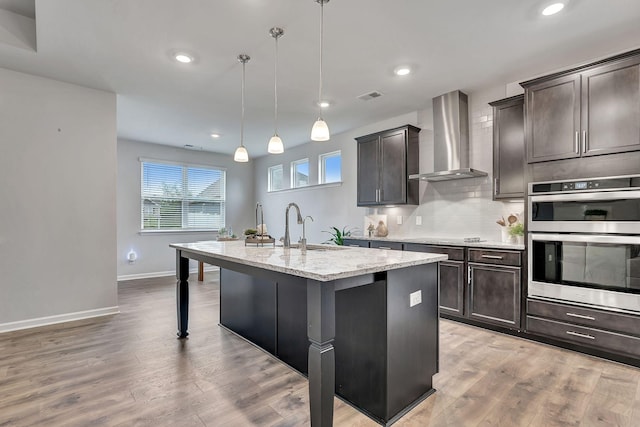 1044 Alta Vista Ln, Smyrna, TN 37167 - kitchen with wall chimney range hood, double oven, a sink, light stone countertops, and a center island with sink