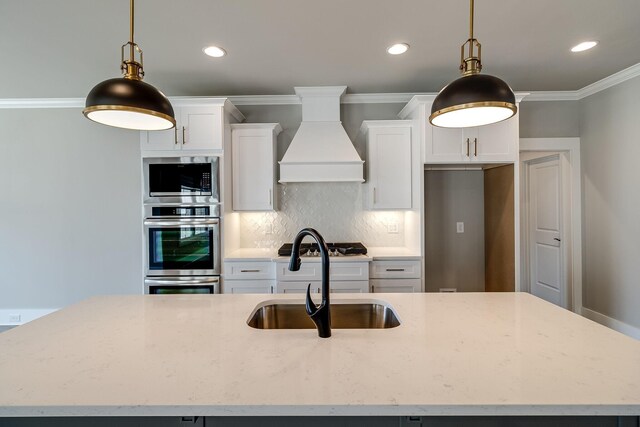 kitchen with a sink, premium range hood, appliances with stainless steel finishes, white cabinets, and crown molding