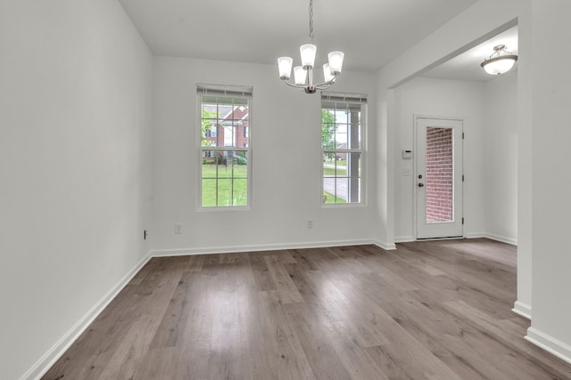 unfurnished dining area with a chandelier, wood finished floors, and baseboards