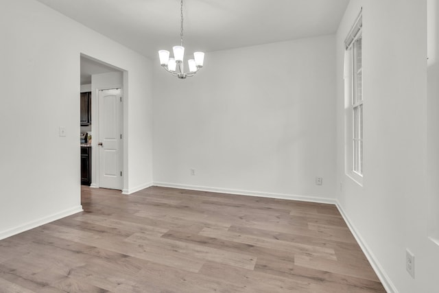 unfurnished dining area with a chandelier, light wood-style floors, and baseboards