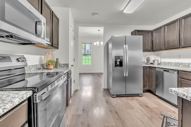 kitchen with stainless steel appliances, dark brown cabinetry, light wood-style flooring, a chandelier, and light stone counters