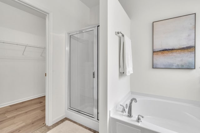 bathroom featuring a shower stall, a walk in closet, a garden tub, wood finished floors, and baseboards
