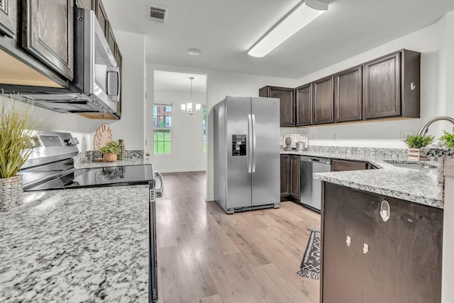 kitchen with stainless steel appliances, a sink, dark brown cabinets, light wood-style flooring, and light stone countertops