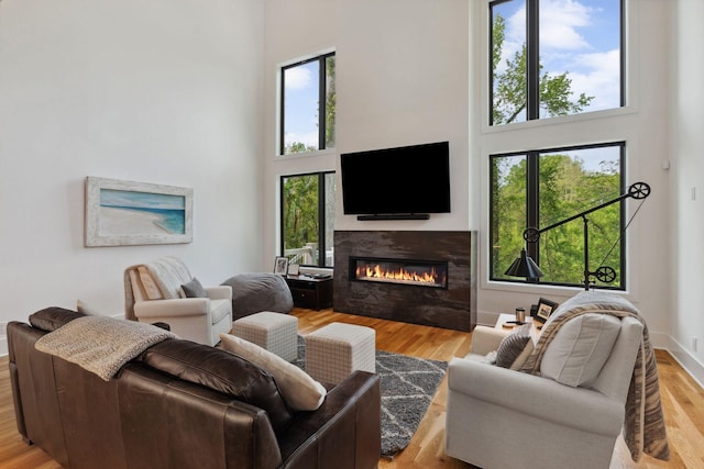 living room with a high ceiling, a glass covered fireplace, and wood finished floors