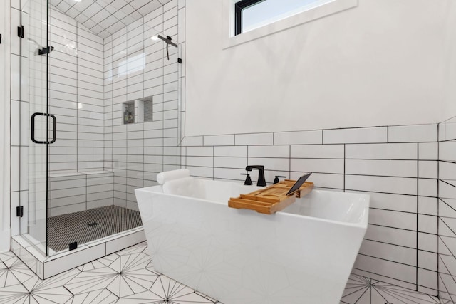 bathroom with tile walls, a shower stall, tile patterned flooring, and a freestanding tub