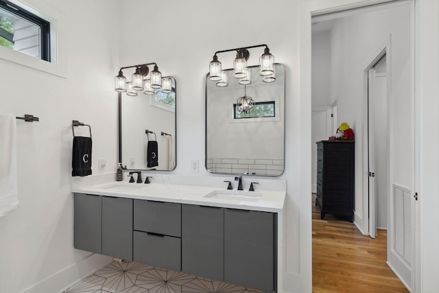 bathroom featuring baseboards, double vanity, a chandelier, and wood finished floors