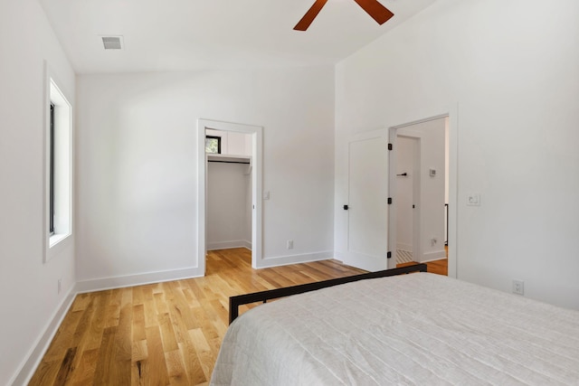 bedroom with light wood-style flooring, a spacious closet, vaulted ceiling, baseboards, and ceiling fan