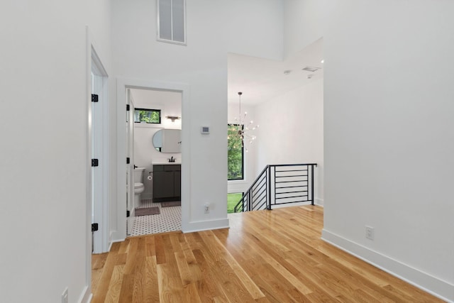 corridor featuring an upstairs landing, light wood-style floors, a chandelier, baseboards, and a high ceiling