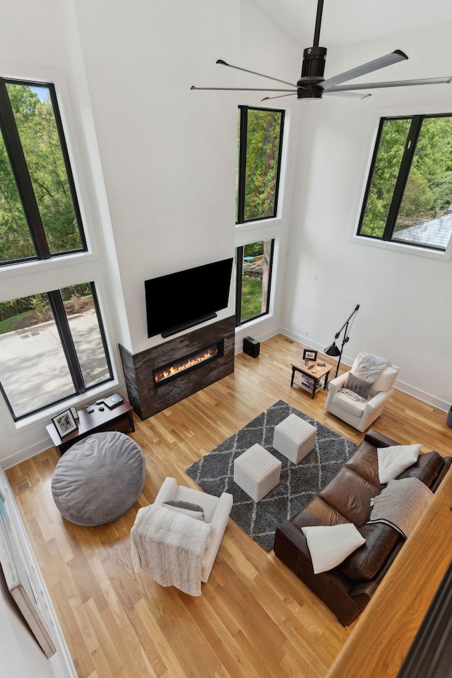 living area featuring a ceiling fan, a warm lit fireplace, and wood finished floors