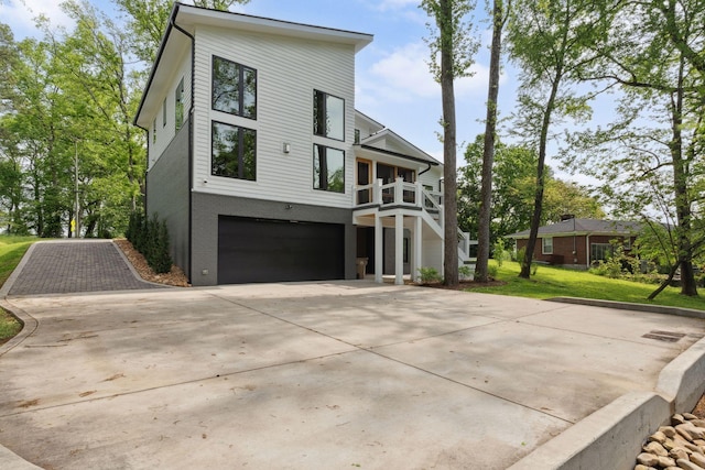 rear view of property featuring a garage, concrete driveway, a yard, and a balcony