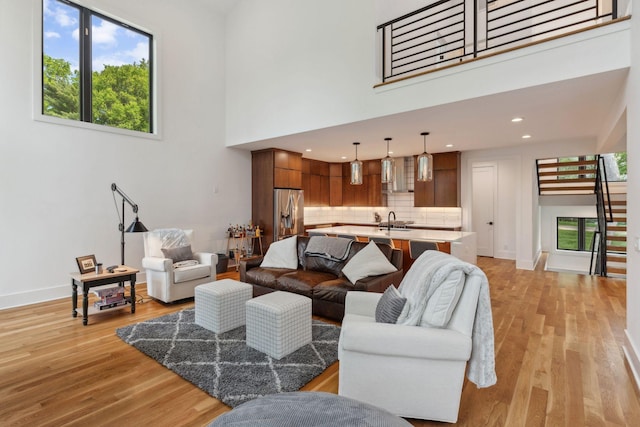 living room with light wood-style flooring, a high ceiling, recessed lighting, and baseboards