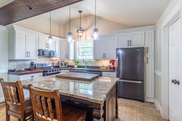 kitchen featuring stainless steel appliances, a sink, tasteful backsplash, a breakfast bar area, and lofted ceiling