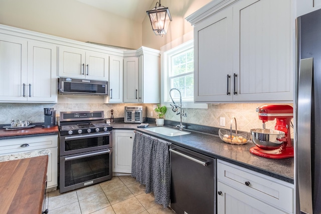 kitchen with appliances with stainless steel finishes, tasteful backsplash, light tile patterned flooring, a sink, and decorative light fixtures