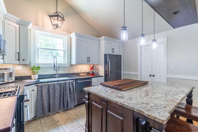 kitchen with appliances with stainless steel finishes, a sink, tasteful backsplash, lofted ceiling, and a center island