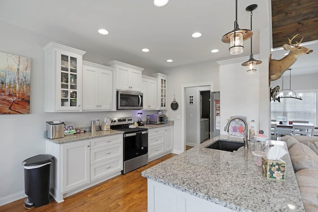 kitchen featuring stainless steel appliances, a sink, white cabinetry, light wood-style floors, and glass insert cabinets