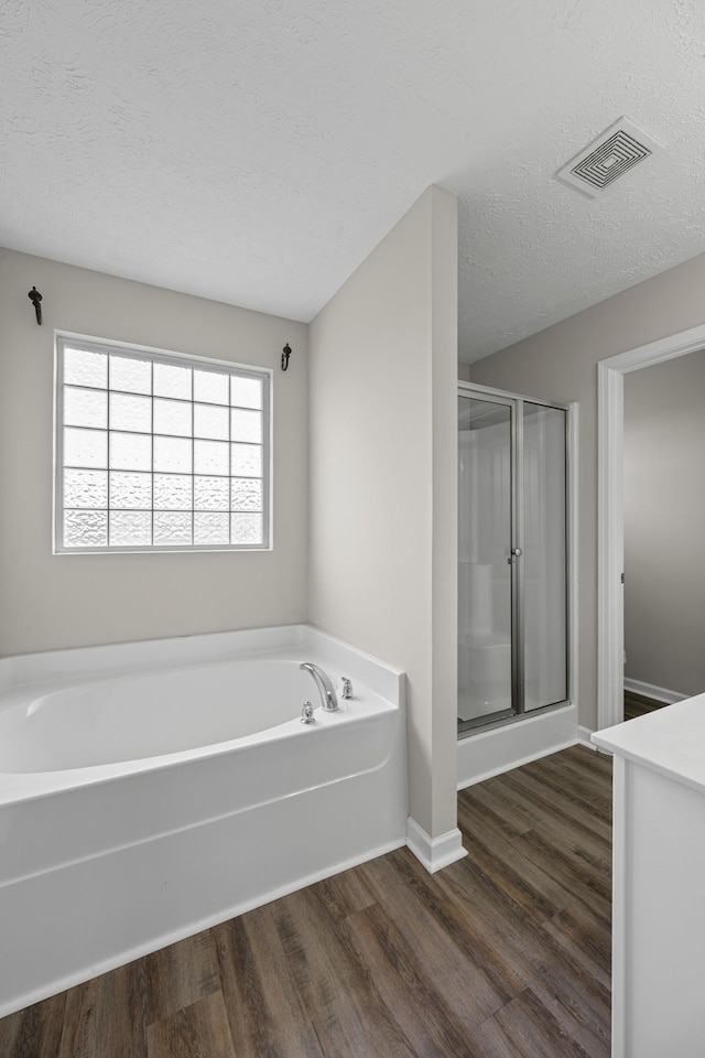 5029 Luker Ln, Antioch, TN 37013 - bathroom featuring wood finished floors, a garden tub, a stall shower, a textured ceiling, and baseboards