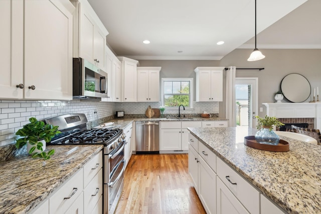 kitchen featuring appliances with stainless steel finishes, a sink, ornamental molding, white cabinets, and decorative backsplash