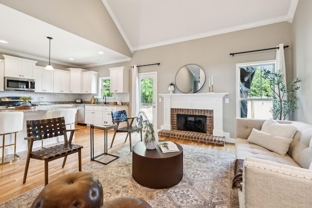 living area featuring ornamental molding, light wood-type flooring, a fireplace, and lofted ceiling