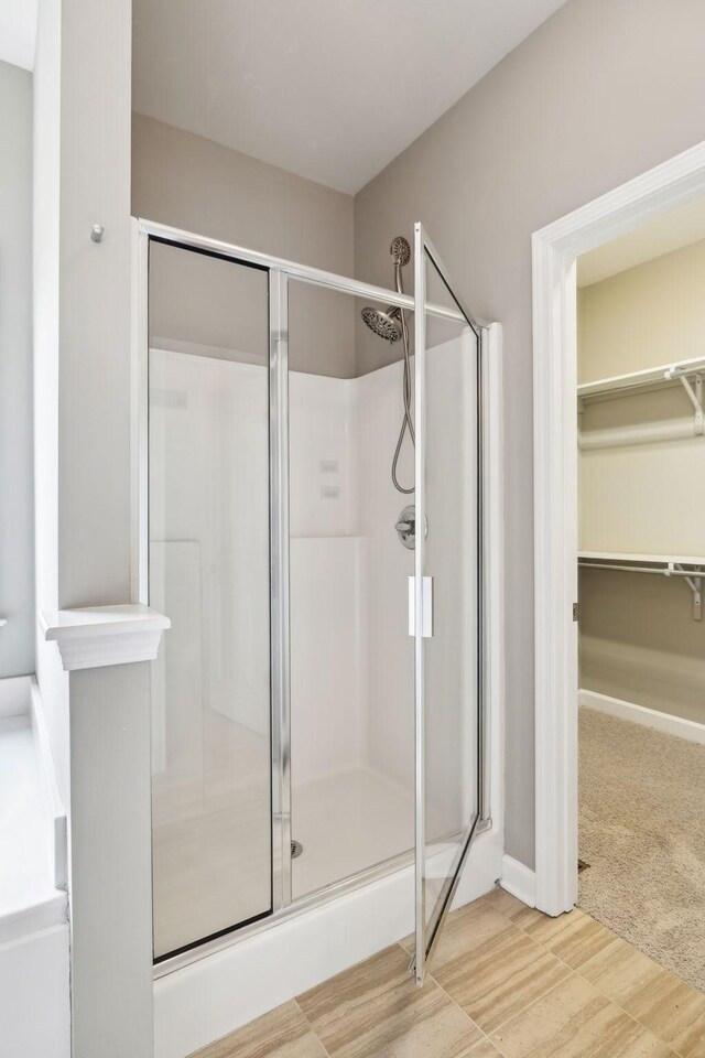 full bath featuring a shower stall, a walk in closet, and wood finished floors