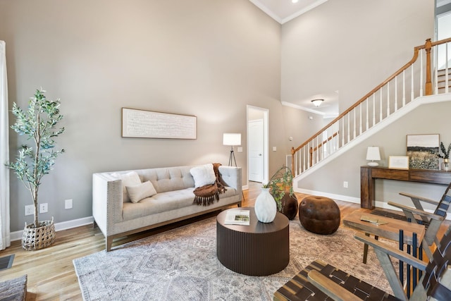 living room featuring crown molding, stairway, wood finished floors, baseboards, and a high ceiling