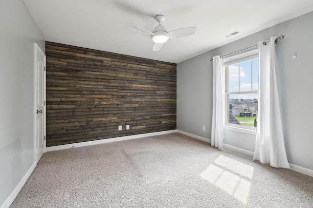 empty room with wood walls, an accent wall, a ceiling fan, and carpet flooring