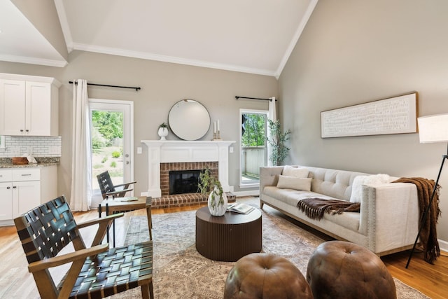 living room with ornamental molding, vaulted ceiling, light wood-style floors, and a brick fireplace