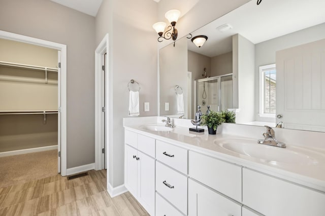 bathroom featuring a shower stall, a spacious closet, double vanity, and baseboards