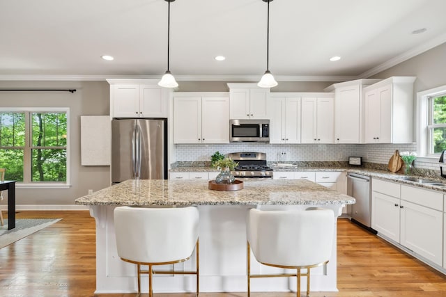 kitchen with appliances with stainless steel finishes, a sink, white cabinetry, a kitchen island, and backsplash