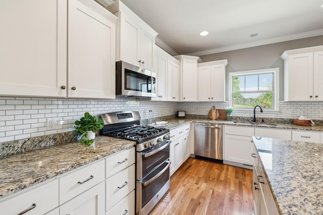 kitchen with stainless steel appliances, a sink, ornamental molding, white cabinetry, and light wood-style floors