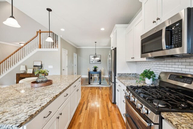 kitchen featuring stainless steel appliances, ornamental molding, light wood-style flooring, white cabinets, and backsplash