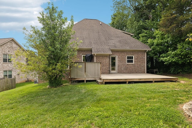 back of house with roof with shingles, brick siding, a wooden deck, and a yard