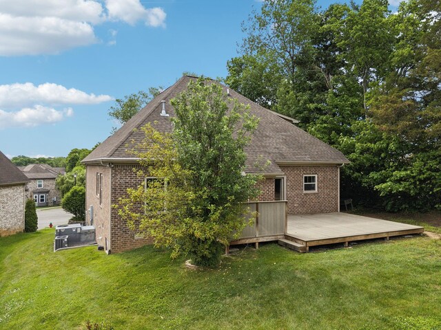 back of house featuring brick siding, a wooden deck, a lawn, and a shingled roof