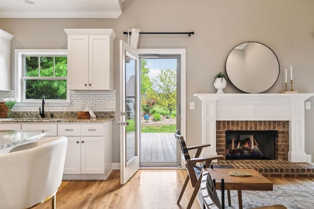 kitchen featuring a sink, light wood-style floors, light stone counters, white cabinets, and tasteful backsplash