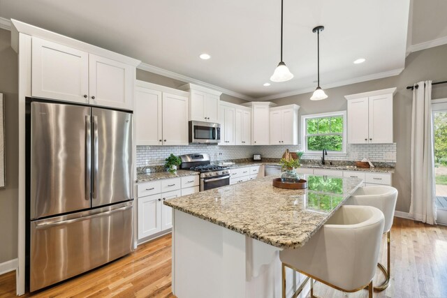 kitchen with stainless steel appliances, white cabinets, crown molding, light wood finished floors, and a kitchen island