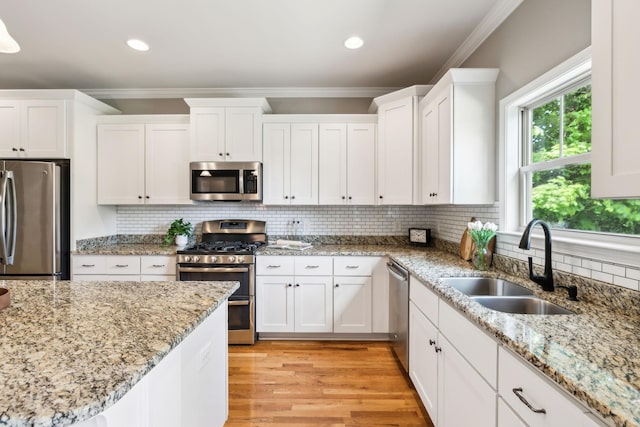 kitchen featuring appliances with stainless steel finishes, a sink, ornamental molding, white cabinets, and backsplash