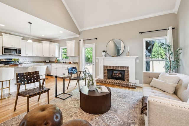 living area with light wood finished floors, ornamental molding, a brick fireplace, and vaulted ceiling