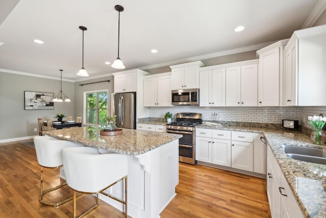 kitchen with appliances with stainless steel finishes, ornamental molding, backsplash, a center island, and white cabinets