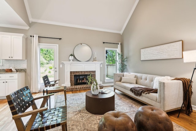 living area featuring crown molding, light wood finished floors, lofted ceiling, and a brick fireplace