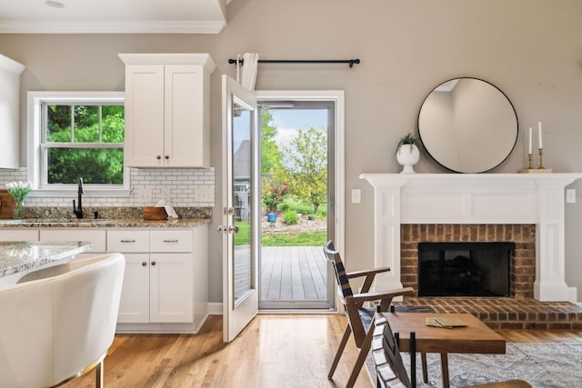 kitchen with a sink, light wood finished floors, light stone countertops, white cabinetry, and decorative backsplash