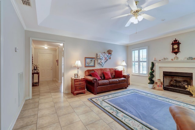 living room with a tray ceiling, ceiling fan, light tile patterned floors, baseboards, and crown molding