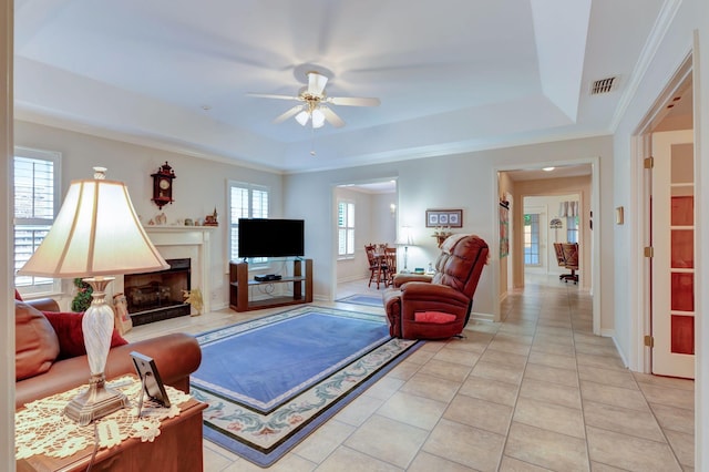 living area with a tray ceiling, ceiling fan, light tile patterned floors, a high end fireplace, and crown molding
