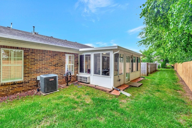 rear view of house with central AC unit, a sunroom, brick siding, and a shingled roof