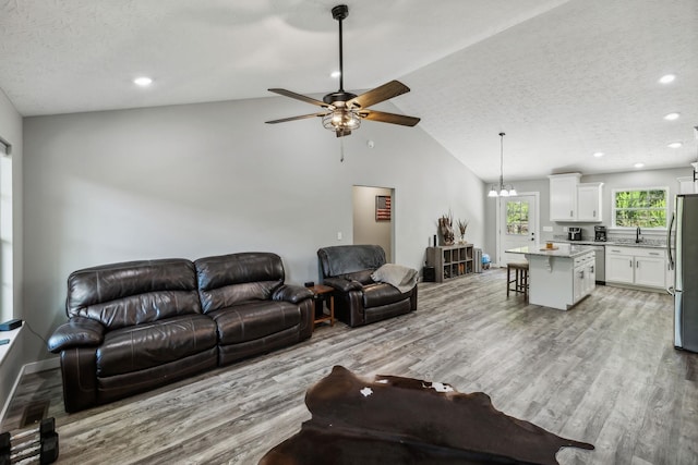 living area with light wood-style flooring, lofted ceiling, ceiling fan, recessed lighting, and a textured ceiling
