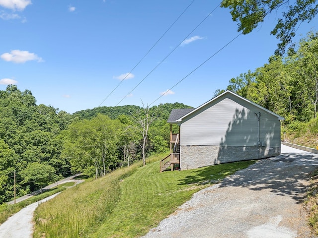 view of home's exterior featuring a forest view, stairs, stone siding, and a lawn