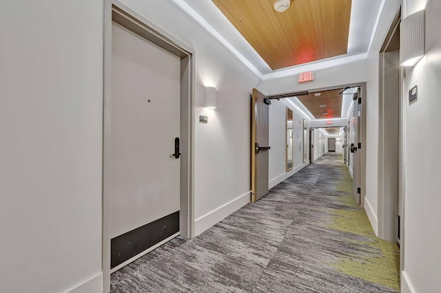 corridor featuring wooden ceiling, a tray ceiling, baseboards, and carpet floors