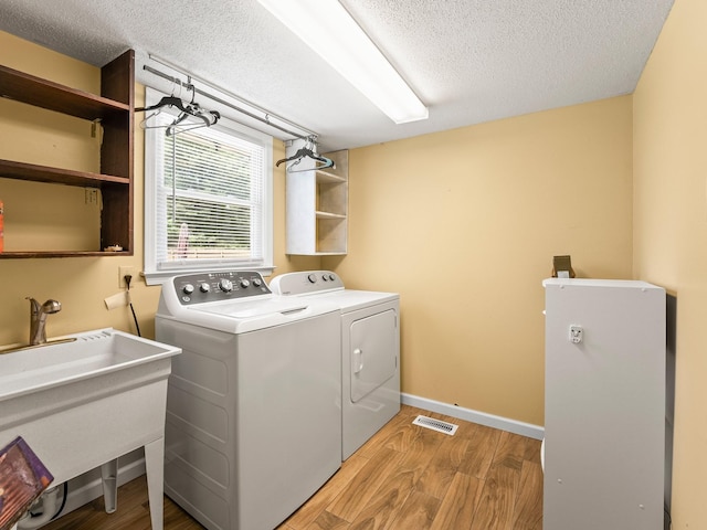 laundry area featuring light wood finished floors, washer and dryer, a textured ceiling, and baseboards
