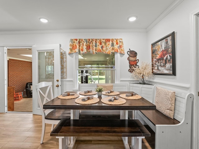 dining room with breakfast area, crown molding, light wood finished floors, and a wainscoted wall