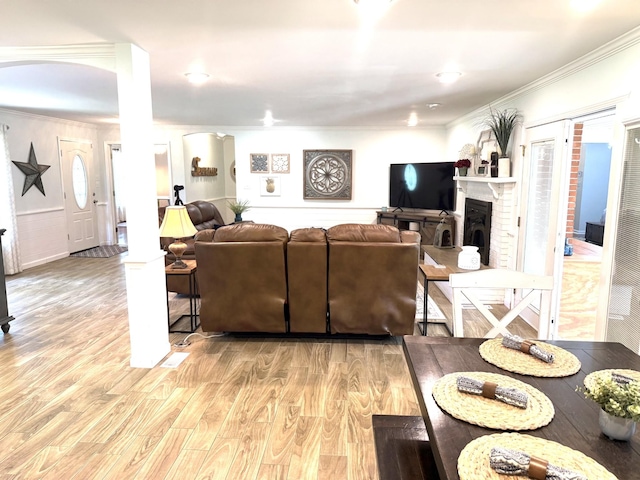 living room with ornamental molding, light wood-type flooring, and a brick fireplace
