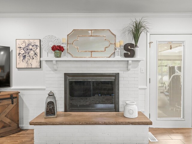 detailed view of crown molding, wood finished floors, and a brick fireplace