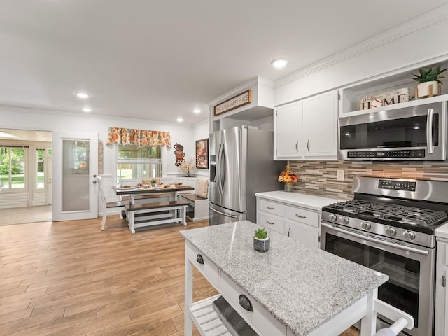 kitchen featuring stainless steel appliances, healthy amount of natural light, tasteful backsplash, ornamental molding, and white cabinets